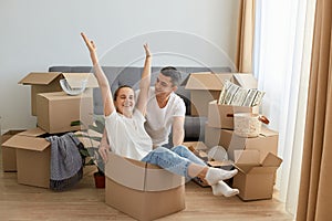 Indoor shot of happy couple having fun with cardboard boxes in new house at moving day, satisfied family with positive emotions