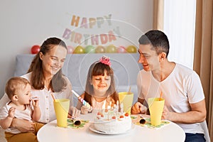 Indoor shot of happy family spending time together, celebrating birthday, smiling happily, sitting at table with big delicious