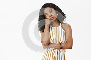 Indoor shot of intense bored and annoyed good-looking dark-skinned female in trendy striped yellow overalls leaning head