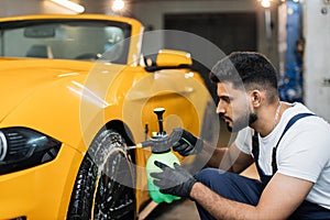 Indoor shot of male worker in overalls, washing the car wheels rims