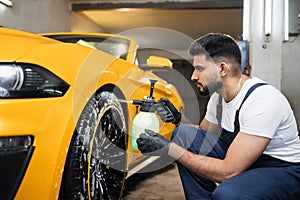 Indoor shot of male worker in overalls, washing the car wheels rims