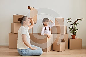 Indoor shot of mother with daughter posing surrounded with packages with stuff, little girl and woman making ship with flag during