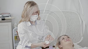 Indoor shot of pretty woman cosmetologist applying to her female client anti aging mask or cream. Young girl relaxing