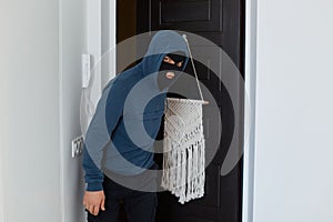 Indoor shot of robber wearing blue hoodie and black mask, breaking apartment to steal something, going inside for stealing someone