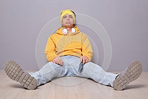 Indoor shot of sad unhappy man wearing beanie hat, yellow hoodie and jeans, looking at camera with pout lips, expressing sorrow