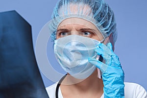 Indoor shot of shocked female doctor examining patient`s x-ray, talking via phone with her colleague, portrait of beautiful young