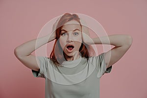 Indoor shot of shocked scared woman keeping head in hands, staring at camera with bugged eyes