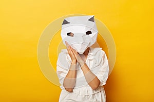 Indoor shot of sleepy anonymous woman wearing dress and paper cat mask standing with palms near cheek, having nap, being tired and