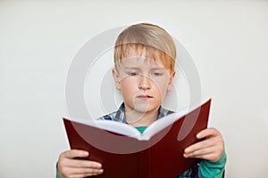 A indoor shot of small schoolboy with fair hair holding a book in his hands. A little boy reading a book isolated over white backg
