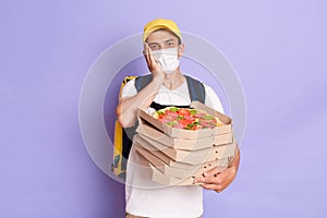 Indoor shot of tired delivery man in protective mask holding pizza boxes, delivering food orders during pandemic, having flu