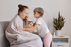 Indoor shot of unhealthy woman drinking tea and suffering runny nose, cute child hugging sick mother, taking care of her mom,