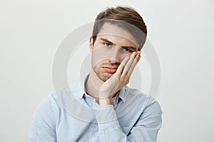 Indoor shot of upset irritated caucasian guy leaning on palm and sighing at camera, being bored and fed up of annoying