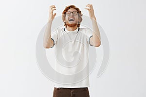 Indoor shot of upset redhead man in despair screaming and yelling from painful feelings and regret tilting head raising