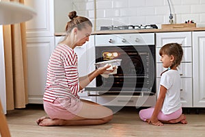 Indoor shot of woman and female child wearing casual clothing sitting on floor and smelling spoiled dessert, expressing negative