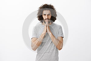 Indoor shot of worried hoping mature brother with beard and curly hair, holding hands in pray over mouth and focusing at