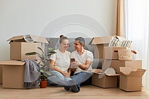 Indoor shot of young couple in love moving in a new apartment, sitting on the floor near, planning to redecorate their new home,