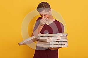 Indoor shot of young handsome delivery man with bad smell spoiled pixxa, male holding carton boxes, posing isolated over yellow