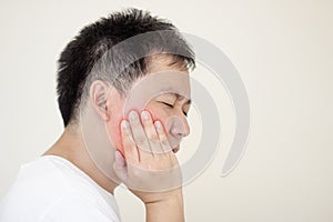 Indoor shot of young male feeling pain, holding his cheek with hand, suffering from bad toothache.