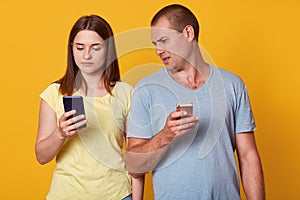 Indoor shot of young marrieds with mobile phones, demonstrates posted photos in social networks, browses in internet. Calm