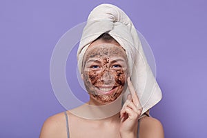 Indoor shot of young smiling attractive woman applying brown cosmetic mask on her face, cleansing her skinat home, usiong