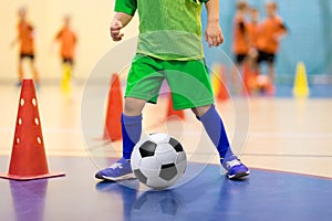 Indoor soccer young player with a soccer ball in a sports hall. Player in green uniform. Sport background.