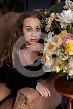 Indoor vertical portrait of a beautiful girl surrounded by peonies