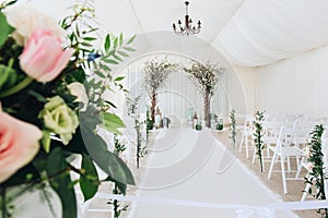 Indoor wedding ceremony with white wedding arch decorated with flowers and big white candles