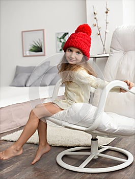 Indoor winter portrait of a little girl in a warm cozy clothes: red knitted winter hat and white kintted dress