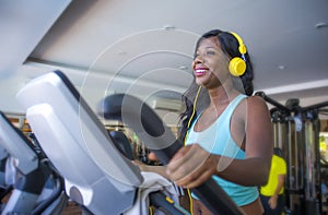 Indoors gym portrait of young attractive and happy black african American woman with headphones training elliptical machine workou
