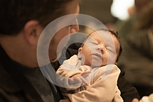 Indoors lifestyle portrait of happy father holding his newborn baby girl only a few weeks old sitting on cafe taking care of the