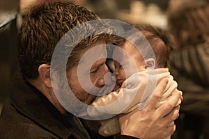 Indoors lifestyle portrait of happy father holding his newborn baby girl only a few weeks old sitting on cafe taking care of the