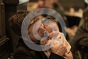 Indoors lifestyle portrait of happy father holding his newborn baby girl only a few weeks old sitting on cafe taking care of the