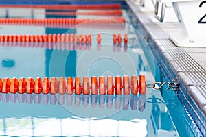 Indoors, orange lane dividers stretch across calm swimming pool water, marking lanes
