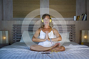 Indoors portrait of beautiful and fit healthy woman 30s practicing yoga listening to music with headphones in bed posing calm and