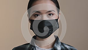 Indoors portrait close facial expression female face asian race woman ill serious girl in black protective medical mask