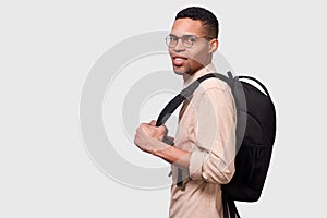 Indoors portrait of handsome young Afro man student with backpack standing over whiet studio background. Young businessman wearing