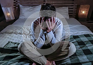 Indoors portrait of young desperate and depressed man at home bedroom sitting on bed sad and confused suffering pain and depressio