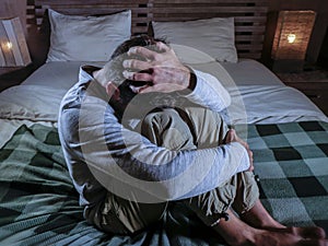Indoors portrait of young desperate and depressed man at home bedroom sitting on bed sad and confused suffering pain and depressio