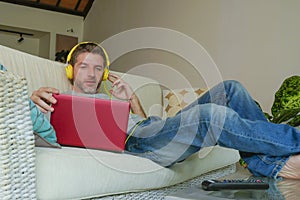 Indoors portrait of young happy relaxed and attractive man lying at home sofa couch with headset and laptop listening to internet