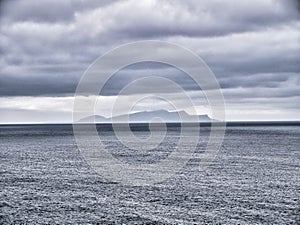 With an induced grain effect on a cold, grey, overcast day, a view across a calm sea to the Shetland island of Foula