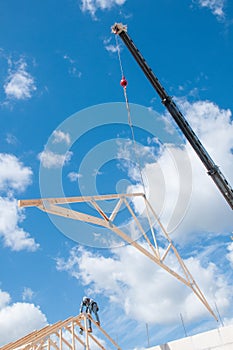 Industial crane, moving a wood, roof truss to be secured by a contractor