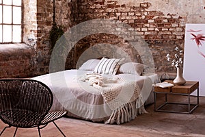 industrail bedroom interior with flowers on wooden table and red brick wall. Real photo