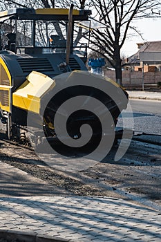 Industrial asphalt paver machine laying fresh asphalt on road construction site on the street. A Paver finisher placing