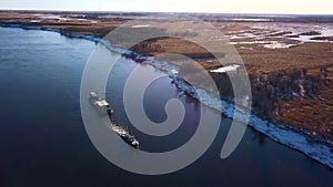 Industrial background with a barge and a river with snowy shore. Clip. Cargo ship transporting goods on a field