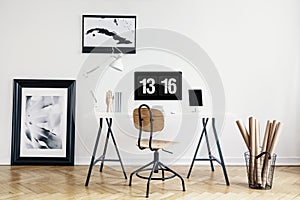 Industrial basket with kraft paper rolls and a framed poster in a white, minimalist home office interior of a freelancer architect