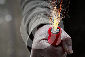 Industrial battery in a man fist from which shoot lightning and smoke clouds float away, composite image, concept