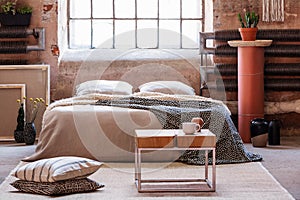 Industrial bedroom interior with blanket on bed and window. Real photo