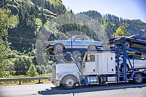 Industrial big rig car hauler semi truck transporting cars on the two level modular semi trailer driving on the road with scenic