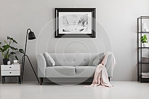 Industrial black floor lamp and a pink blanket on an elegant settee with cushions in a gray living room interior with place for a