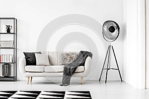 Industrial lamp next to beige couch with blanket and pillows, copy space on empty white wall photo